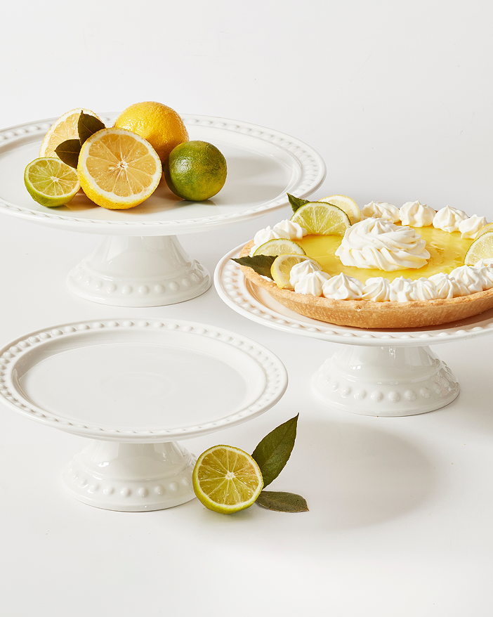 Three white cake stands displaying lemon slices and a pie, arranged elegantly on a table.