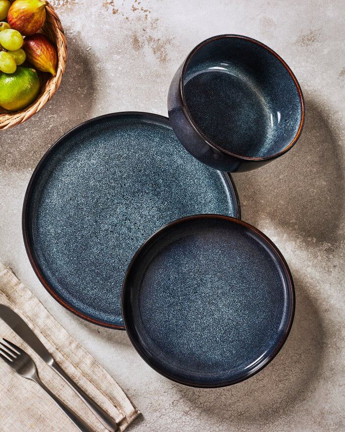 A table set with two blue plates and a bowl filled with assorted fresh fruit